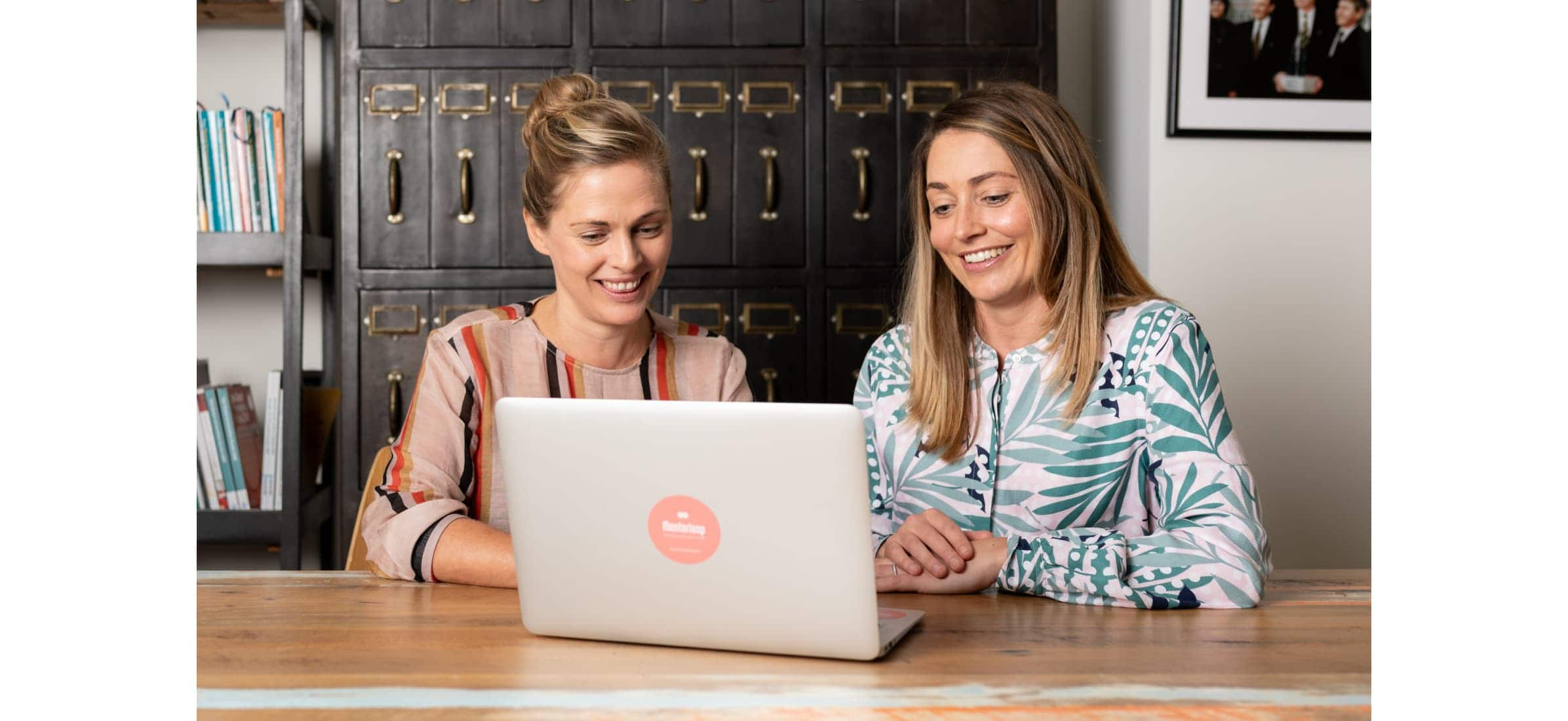 Lucy and Heidi work on a computer together while laughing.